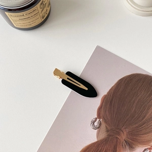 Detail of matte black duckbill hair clip with golden metal base on a minimalist background