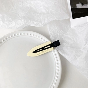 Close-up of beige and black minimalist hair clips on a pearl-edged white plate