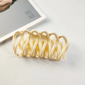 Détail d'une grande pince à cheveux ondulée crème sur un fond de magazine