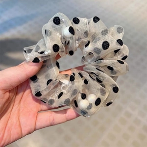 Chic beige mesh scrunchie with black polka dots and white pearls held in hand
