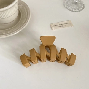 Gros plan d'une pince à cheveux mate kaki au design ondulé évidé sur un bureau épuré