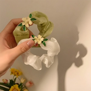 Detail von Organza-Haargummis in Grün und Weiß mit metallischen Blütenverzierungen