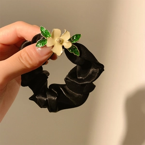Detail eines schwarzen Satin-Haargummis mit einer gelben Emaille-Blume und grünen Blättern