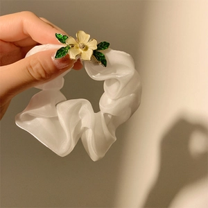 Makroaufnahme von weißem Organza-Haargummi mit gelber Metallblume und Blattverzierung