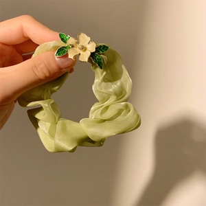 Nahaufnahme eines hellgrünen Organza-Scrunchies mit zarter Metallblume und Blattdetail