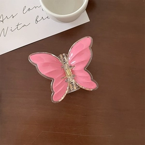 Top view of a sweet pink butterfly hair claw clip with golden spring on dark wood background