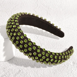 Close-up of a padded headband with green rhinestones on black fabric over white props