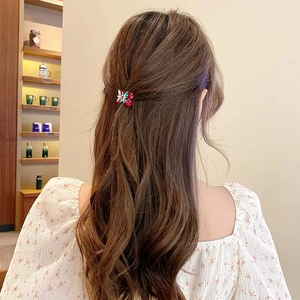 Pince à cheveux cerise avec cristaux rouges et bleus sur longs cheveux bouclés