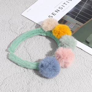 Green plush headband with multi-colored fur balls on a textured grey surface