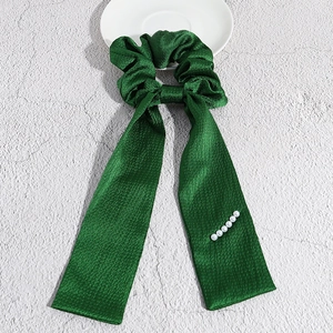 Dettaglio di scrunchie in raso verde con nastri lunghi ed eleganti perle bianche