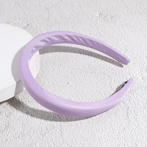 Close-up of a thick purple satin padded headband on a white circular display stand