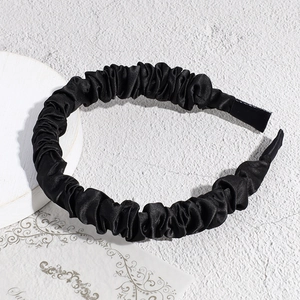 Detailed view of the black pleated satin scrunchie headband on a textured background