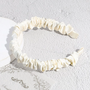 Detail of a creamy pleated satin headband with elegant ruched texture and soft luster