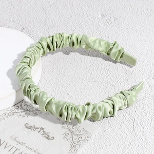 Detail of light green pleated satin headband showing rich texture and wavy glossy fabric