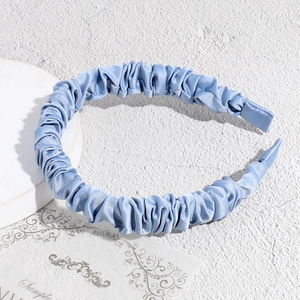 Close-up of pleated light blue satin headband showing smooth silky texture and ruched design