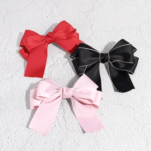 Detailed view of large satin bow hair clips in red, black with gold trim, and pink fabric