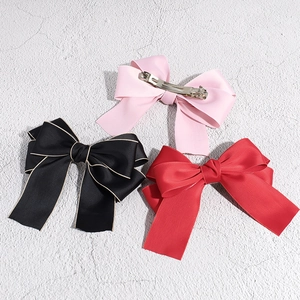 Detailed view of satin bow hair clips in pink, black, and red with silver metal springs