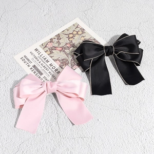 Detail view of pink and black satin bow hair clips with elegant long ribbons on texture