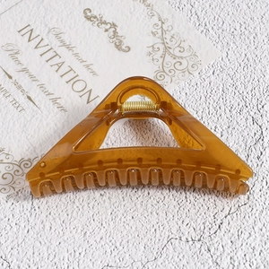 Macro detail of large amber triangle hair claw clip with golden metal spring on white stone
