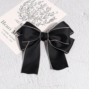 Detail of black satin bow hair clip with elegant gold thread edges on stone background