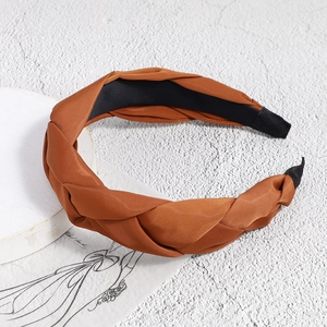 Detail of elegant French braided headband in silk-like caramel fabric on a white pedestal