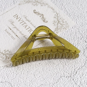 Detail of olive green triangular hair claw clip with golden spring on textured background