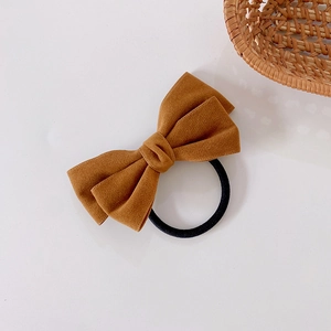 Detail of a velvet-textured caramel bow hair tie with a black elastic telephone wire band