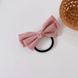 Pink bow hair tie with black elastic cord shown on a minimalist neutral background