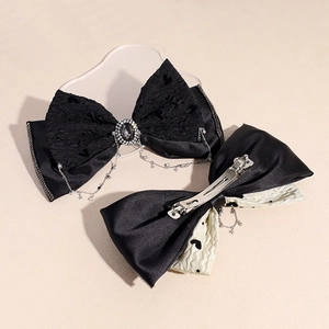 Double-layered black bow hair clips with rhinestones and tassels on a beige background