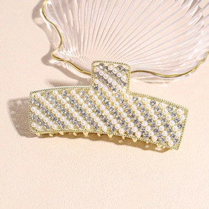 Macro view of gold hair claw clip featuring inlaid pearls and sparkling rhinestones