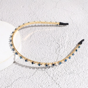 Detail van dunne gouden hoofdband met blauwe kristallen en witte parels op steen