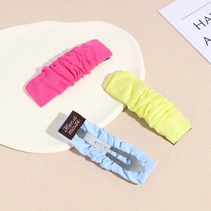 Three-piece pleated fabric hair clips in pink yellow and blue on a white tray