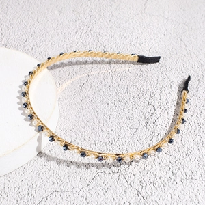 Detail van een dunne gouden metalen haarband met blauwe kristallen en parels