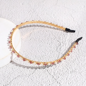 Detail van elegante gouden haarband met witte parels en paarse kristallen op houder