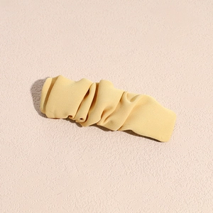 Detailed view of light yellow ruched fabric hair clip with elegant pleated texture