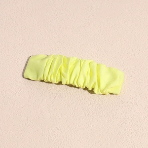 Detail view of yellow ruffled fabric hair clip on a textured light pink background