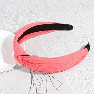 Macro detail of coral pink knitted knotted headband with ribbed texture on white background