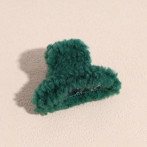 Gros plan d'une pince à cheveux vert foncé en polaire peluche avec texture douce en laine d'agneau