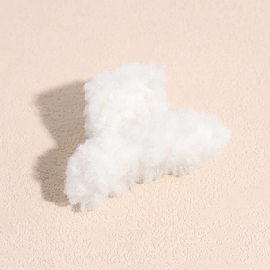 Gros plan sur une pince à cheveux blanche en peluche sur fond de pierre beige