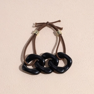 Detailed shot of interlocking black chain links and brown elastic hair tie with gold clasp