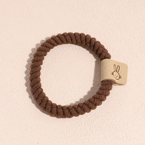 Détail du chouchou en peluche marron foncé avec un patch de lapin sur une surface texturée