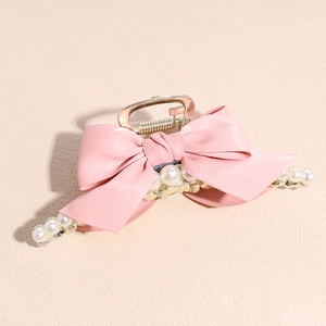Detail of pink silk bow hair claw clip with white pearls on a gold metal base