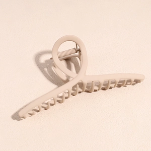Gros plan sur la pince à cheveux beige mat montrant le design torsadé et la texture