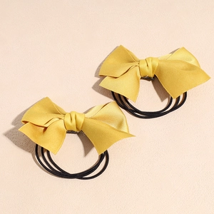 Détail de deux chouchous en satin jaune gingembre avec nœuds et élastiques multi-brins robustes