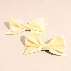 Close-up of a pair of yellow satin ribbon bow hair clips with double-layered texture
