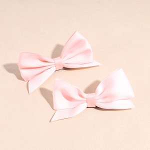 Close-up of two pink satin bow hair clips with soft lighting on a pastel background
