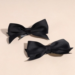 Detail of two black satin bow hair clips with silver metal alligator grip fasteners
