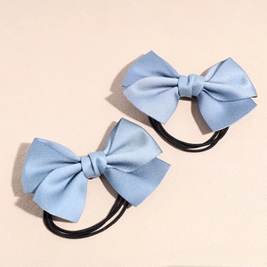 Détail de deux chouchous à nœuds bleu clair avec élastiques noirs sur fond beige uni