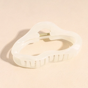 Close-up of cream white acetate hair claw clip with irregular wave design and metal spring