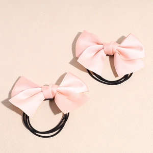 Détail de deux chouchous à nœuds en satin rose avec élastiques sur une surface beige